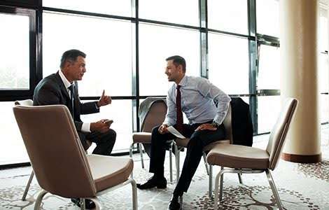 Two business professionals in suits having a discussion in a modern office setting.