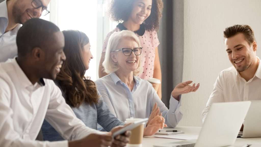 Smiling professionals engaged in a discussion around a laptop in a bright office.